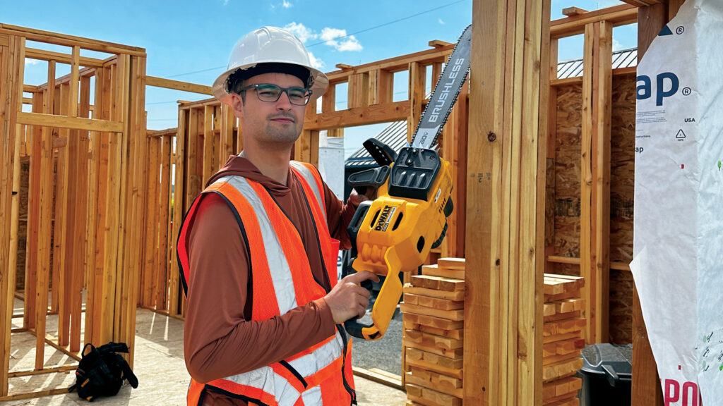 IIE ESF Grantee Hasan Duha Ikiz stands in front of a frame of a house while holding a chainsaw